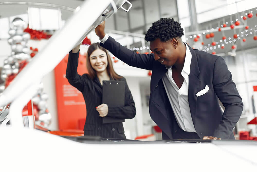 An auto buyer checking under the hood with a car salesman